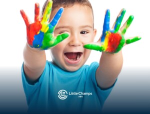 Autistic boy smiling and showing off his painted hands with bright colors.