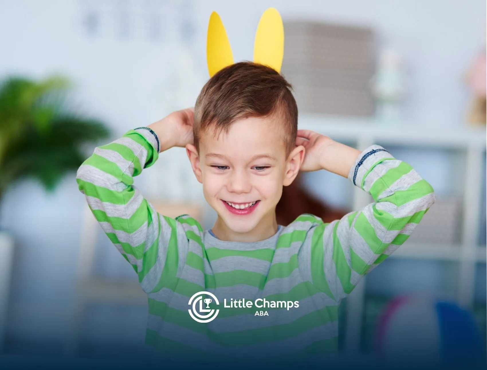 Smiling autistic boy with yellow paper bunny ears on his head.
