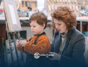 ABA therapist helping a young autistic child put on a paint apron at an art studio in Colorado.