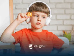 A boy with autism is holding up a block with the letter N while wearing headphones