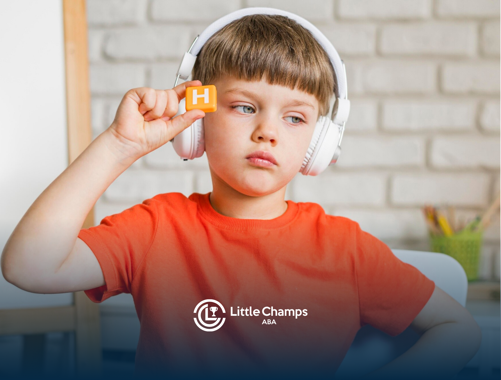 A boy with autism is holding up a block with the letter N while wearing headphones