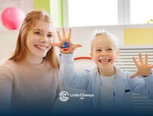 Happy child showing paint-covered hands with BCBA beside her during ABA therapy at a classroom in UT.