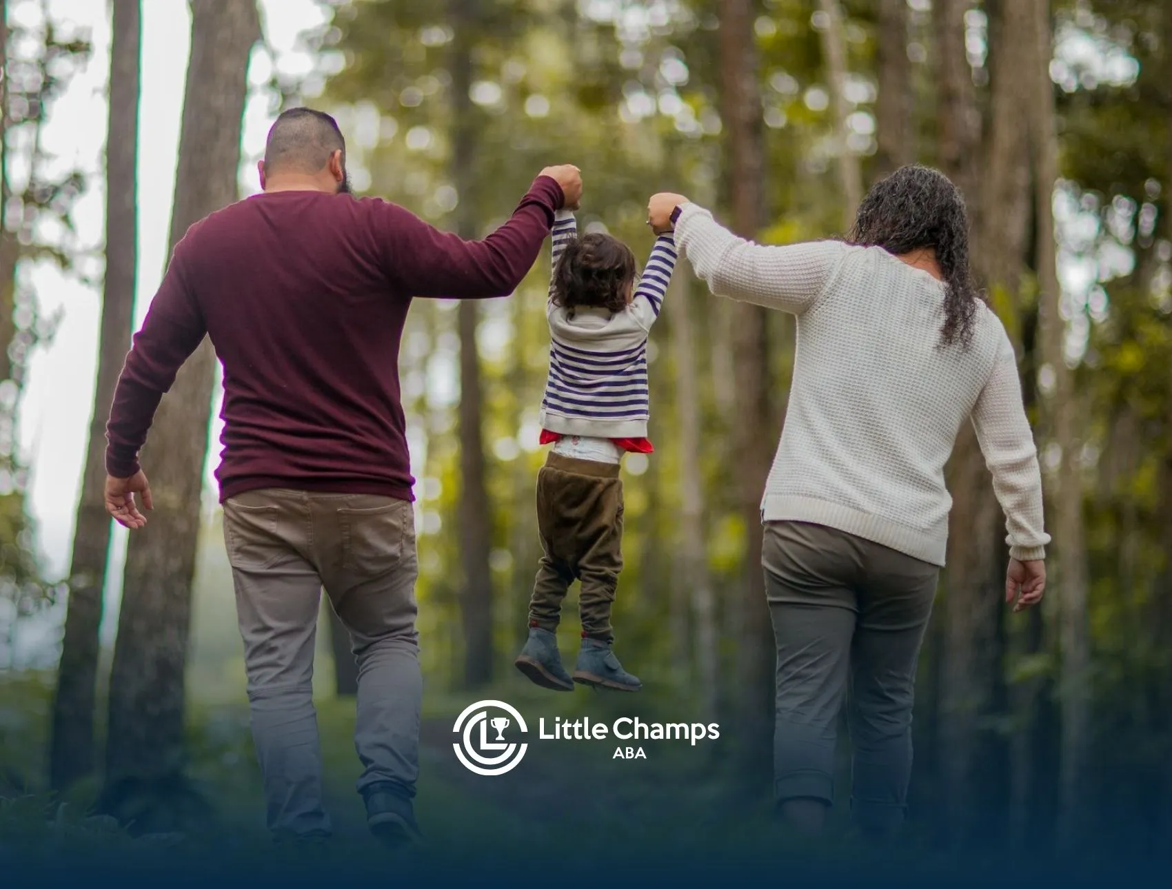 Parents swinging autistic child by arms during forest walk after ABA therapy session in Colorado.