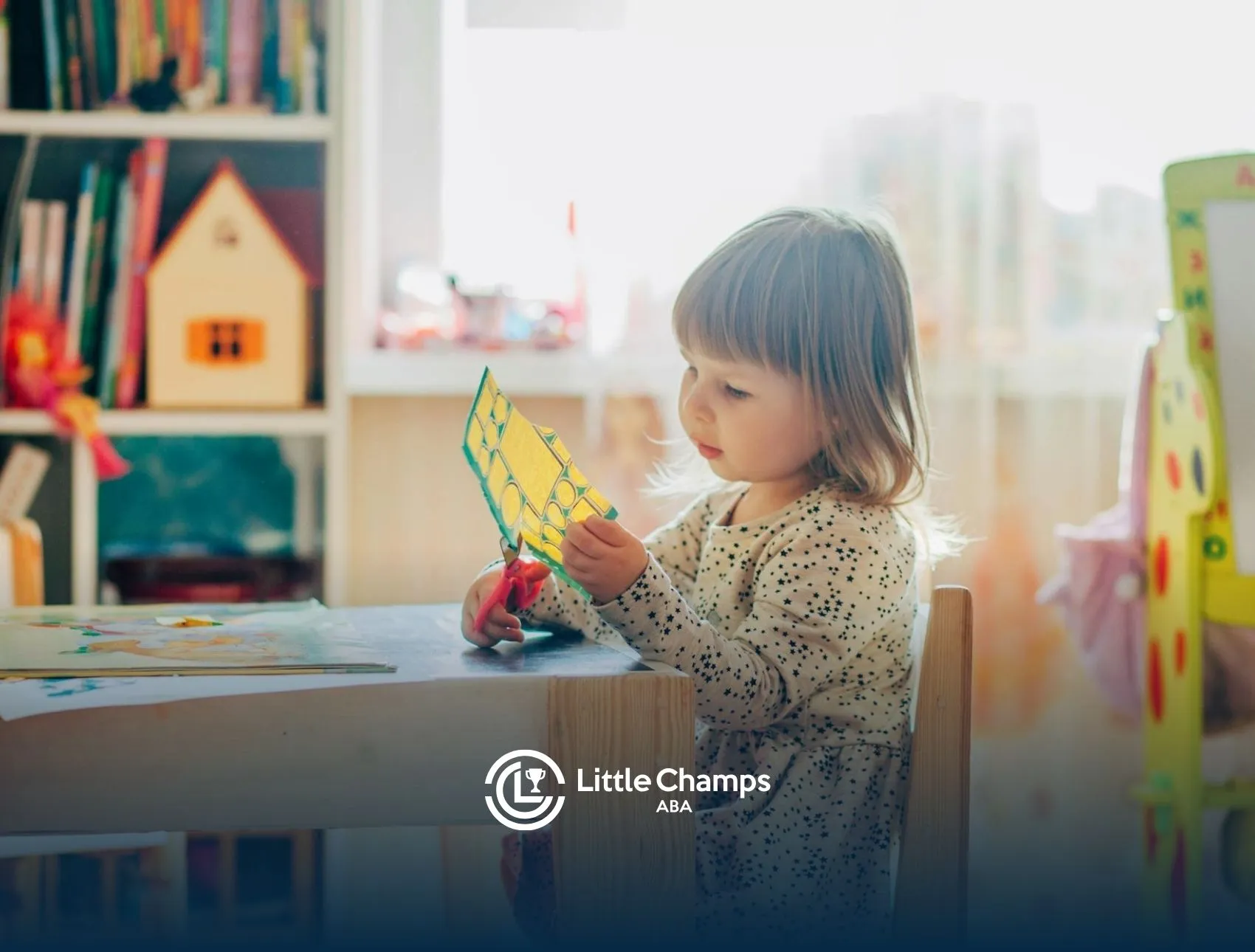 An autistic toddler cutting colored paper with scissors at desk during ABA therapy in Colorado.