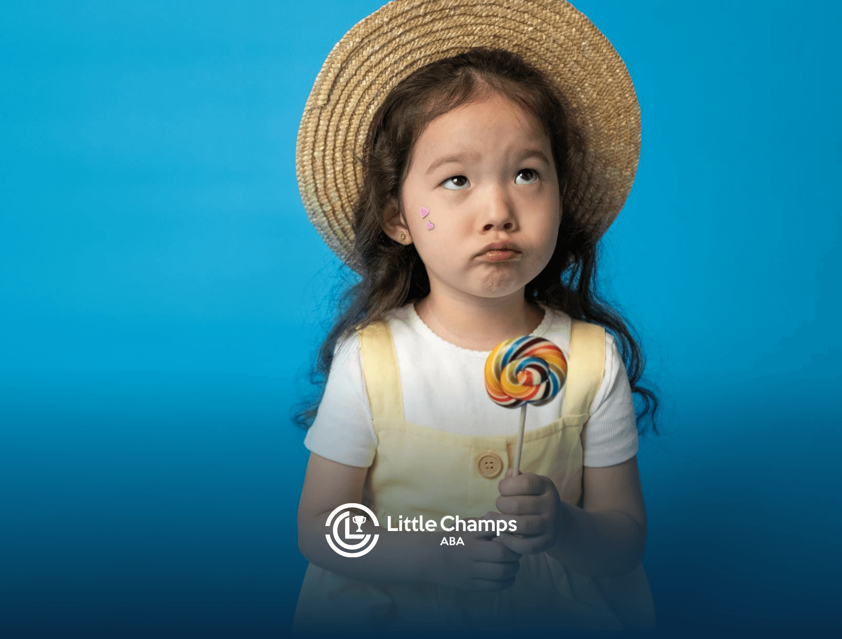 Young autistic girl with hat and lollipop looking up with a pout during school-based ABA therapy in Colorado.