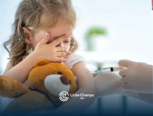 A young child covers their eyes while hugging a teddy bear as they receive a vaccination. The scene conveys a sense of apprehension and comfort.