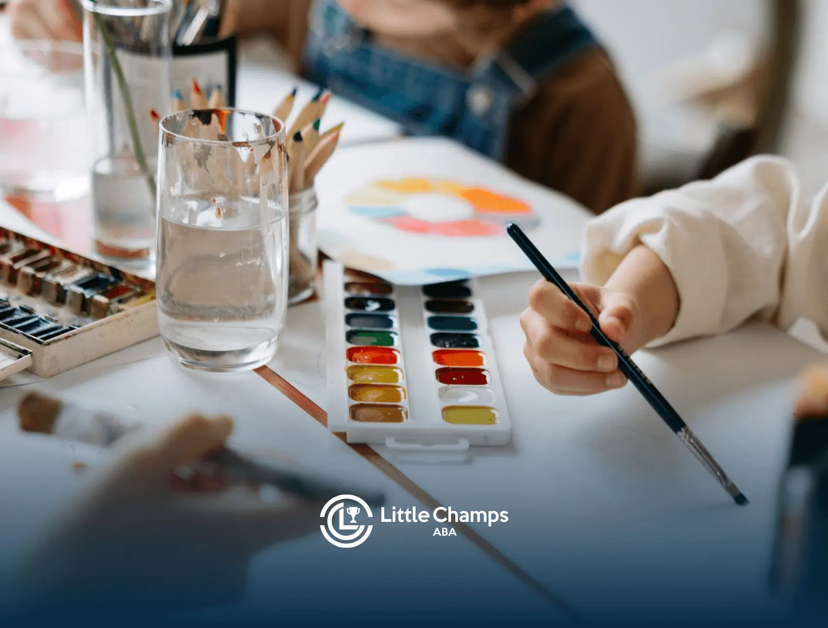 An autistic children painting with watercolors and brushes on a shared table during ABA therapy in Utah.