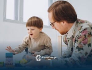 Young boy smiling while building with blocks on the floor beside a supportive ABA therapist.