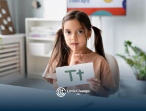Young girl with autism learning letters, holding a "T" flashcard and placing a finger to her lips.