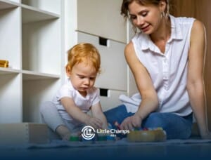 Toddler focused on stacking wooden toys while sitting beside an ABA therapist.