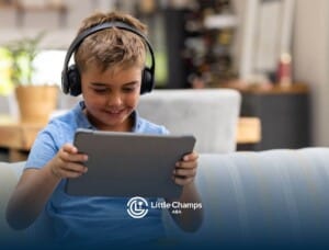 Young boy with autism wearing headphones and smiling while using a tablet on the couch.