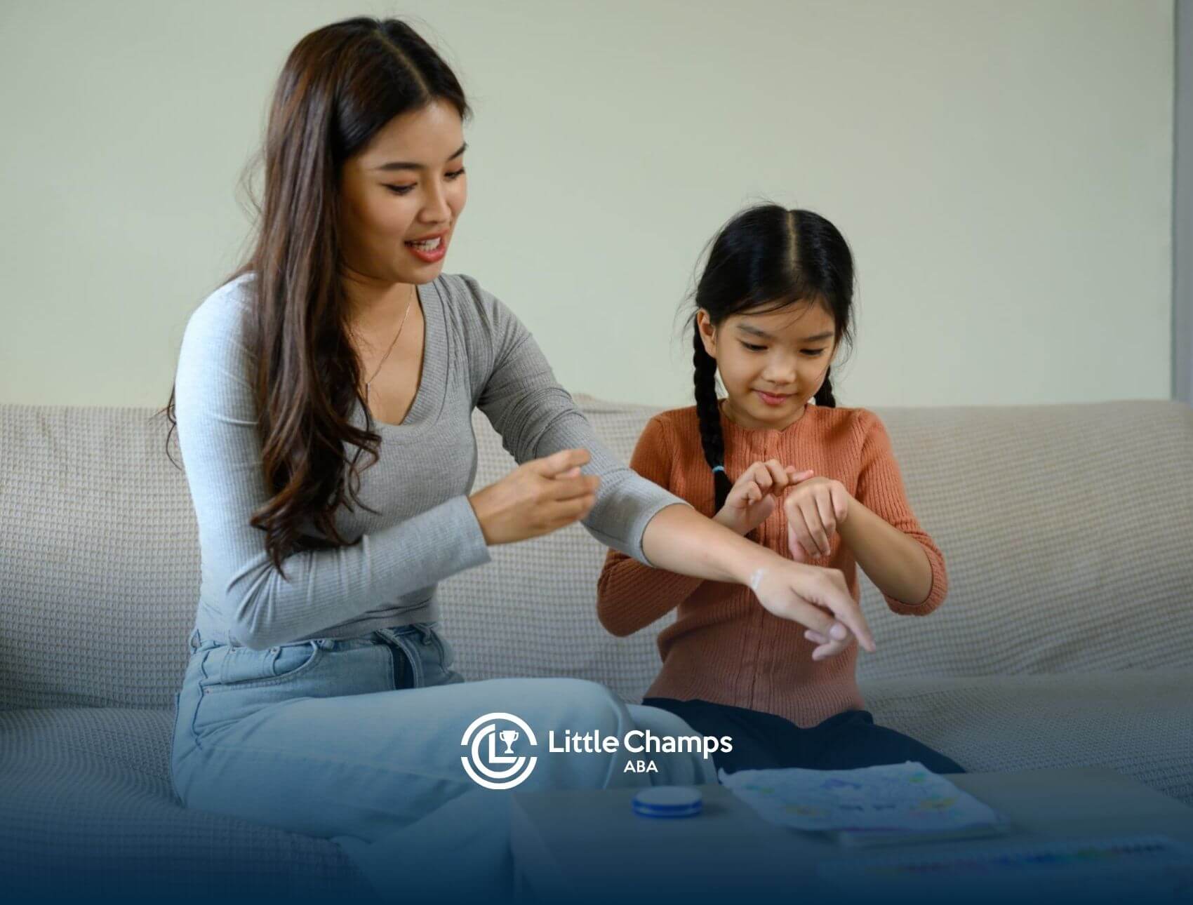 Female ABA therapist and autistic girl applying lotion while sitting on a couch in ABA therapy.