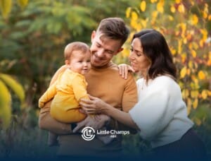 Autistic parents holding baby outdoors in autumn foliage.
