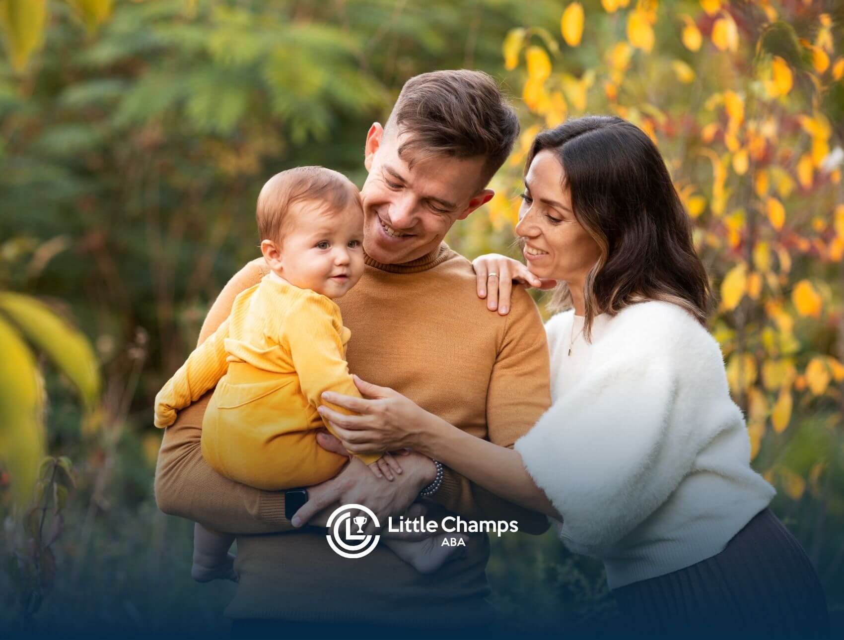 Autistic parents holding baby outdoors in autumn foliage.