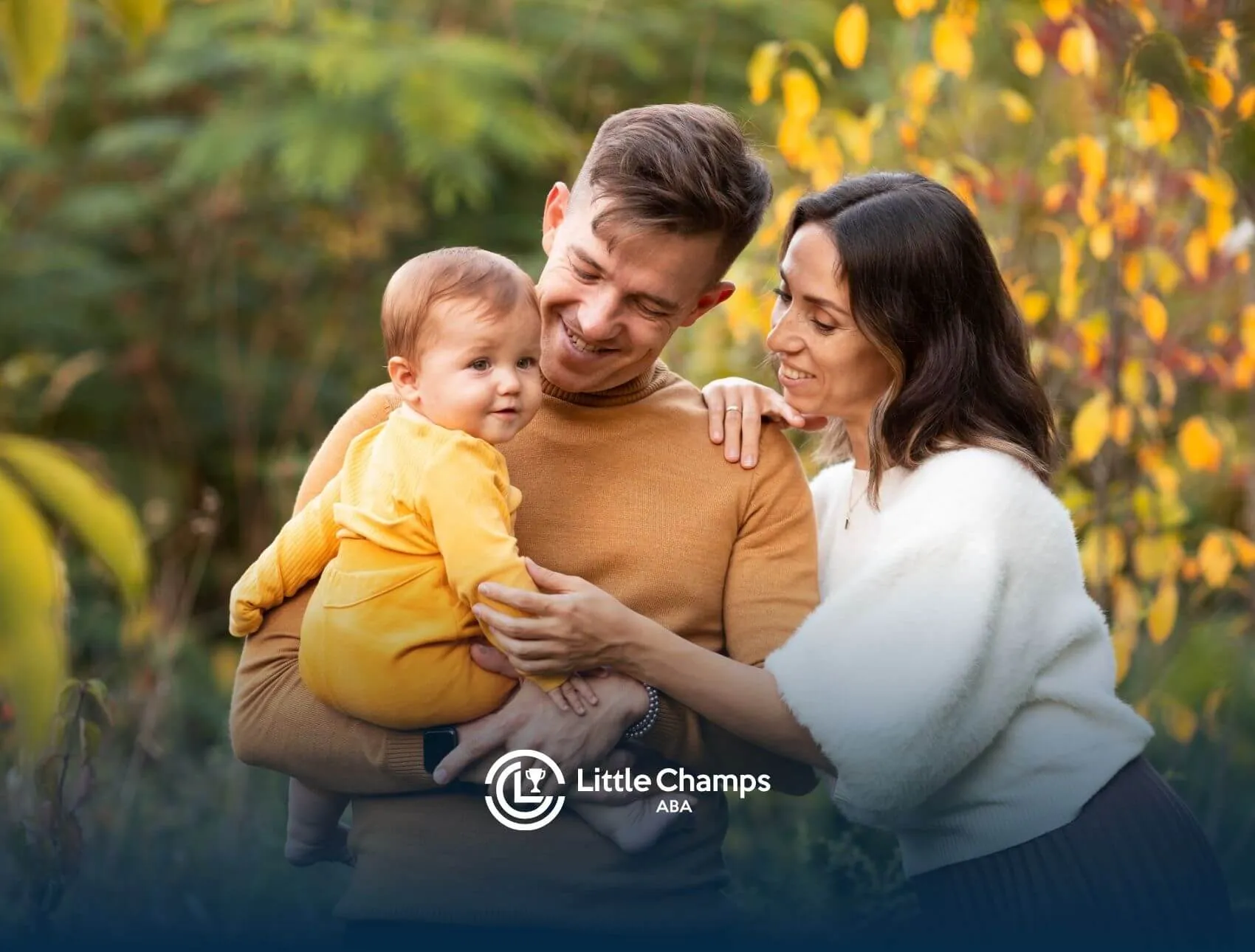 Autistic parents holding baby outdoors in autumn foliage.