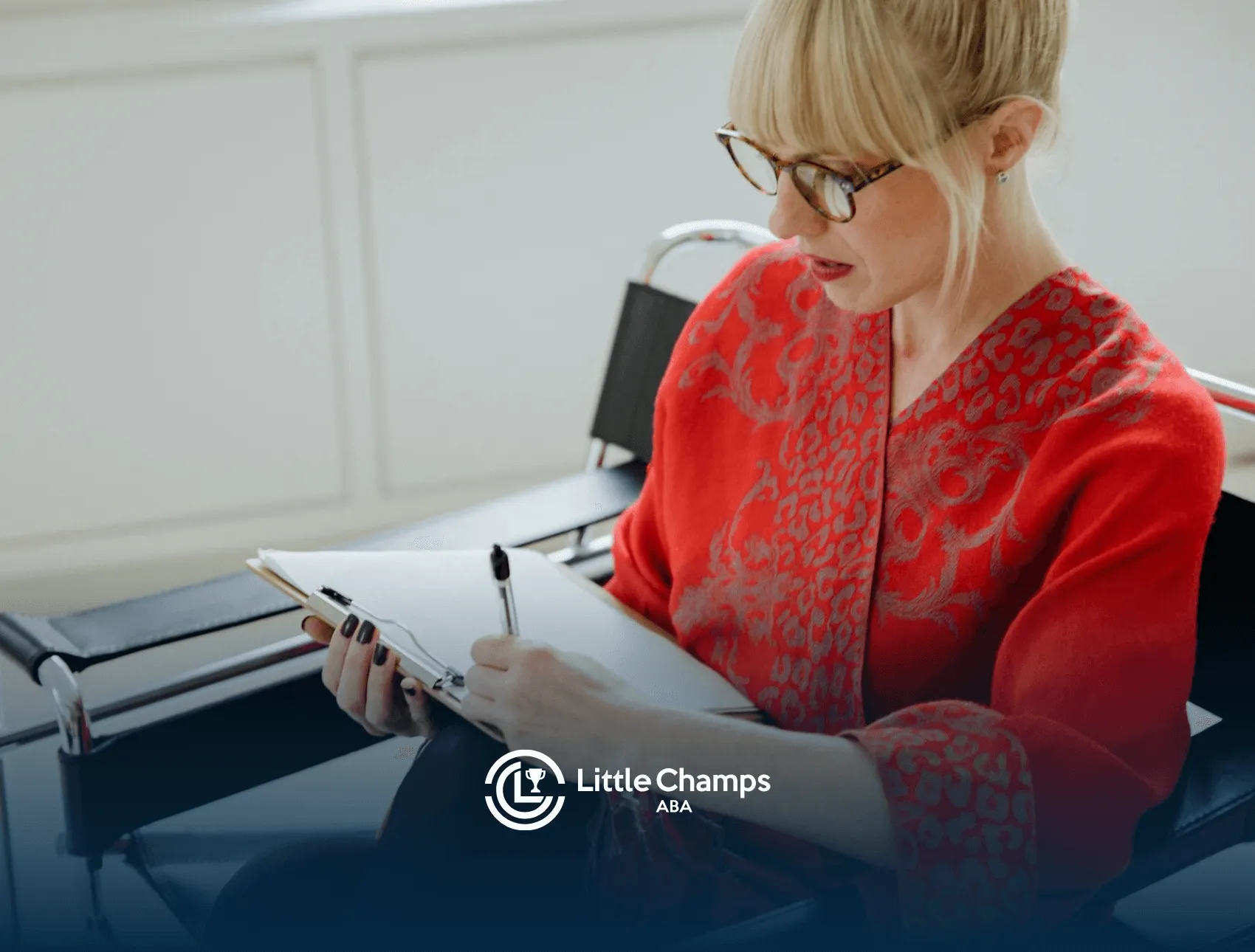 A BCBA in red writing on a clipboard, creating a behavior intervention plan, while seated indoors in Utah.