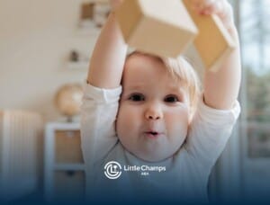 Smiling autistic toddler raising wooden blocks above their head in a cozy room after AB therapy.