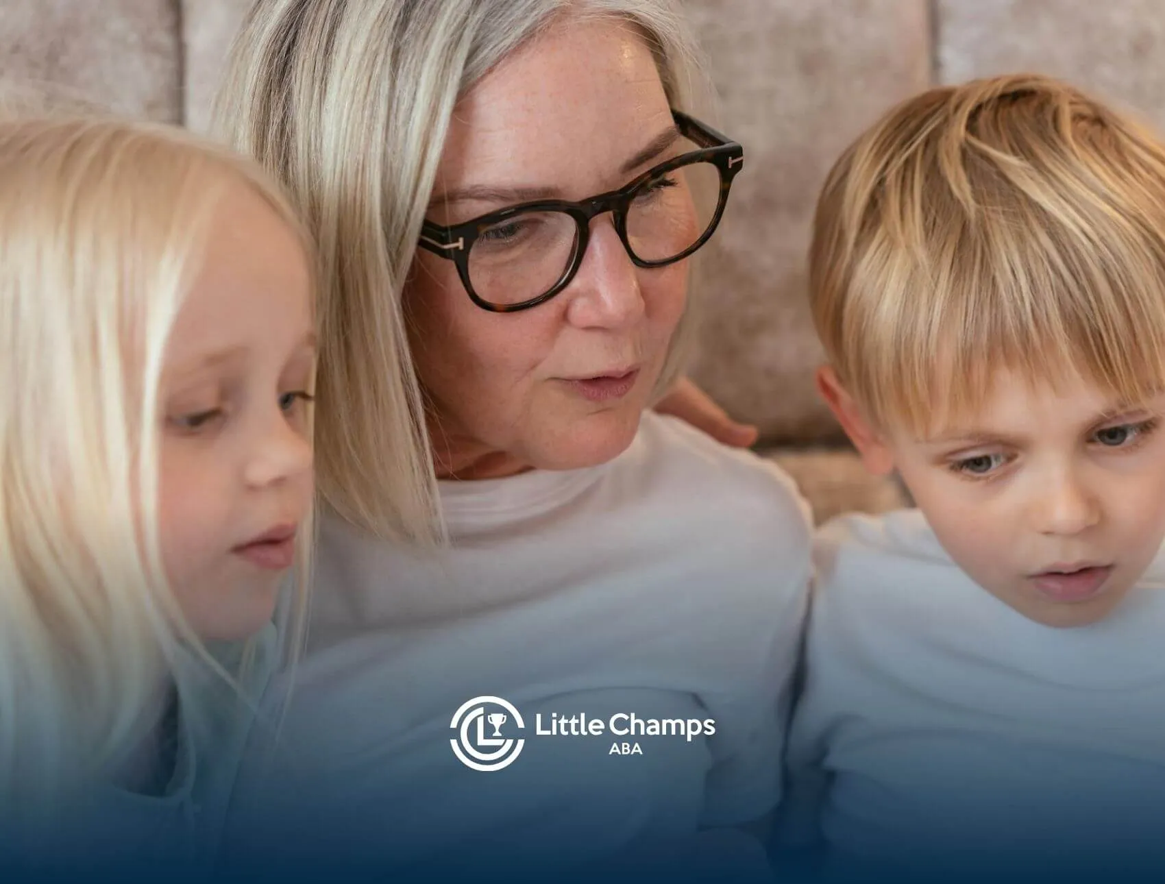 ABA therapist reading with two autistic children sitting closely beside her while looking down.