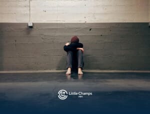 Autistic person sitting barefoot on the floor hugging knees while crying in an empty concrete room in Colorado.