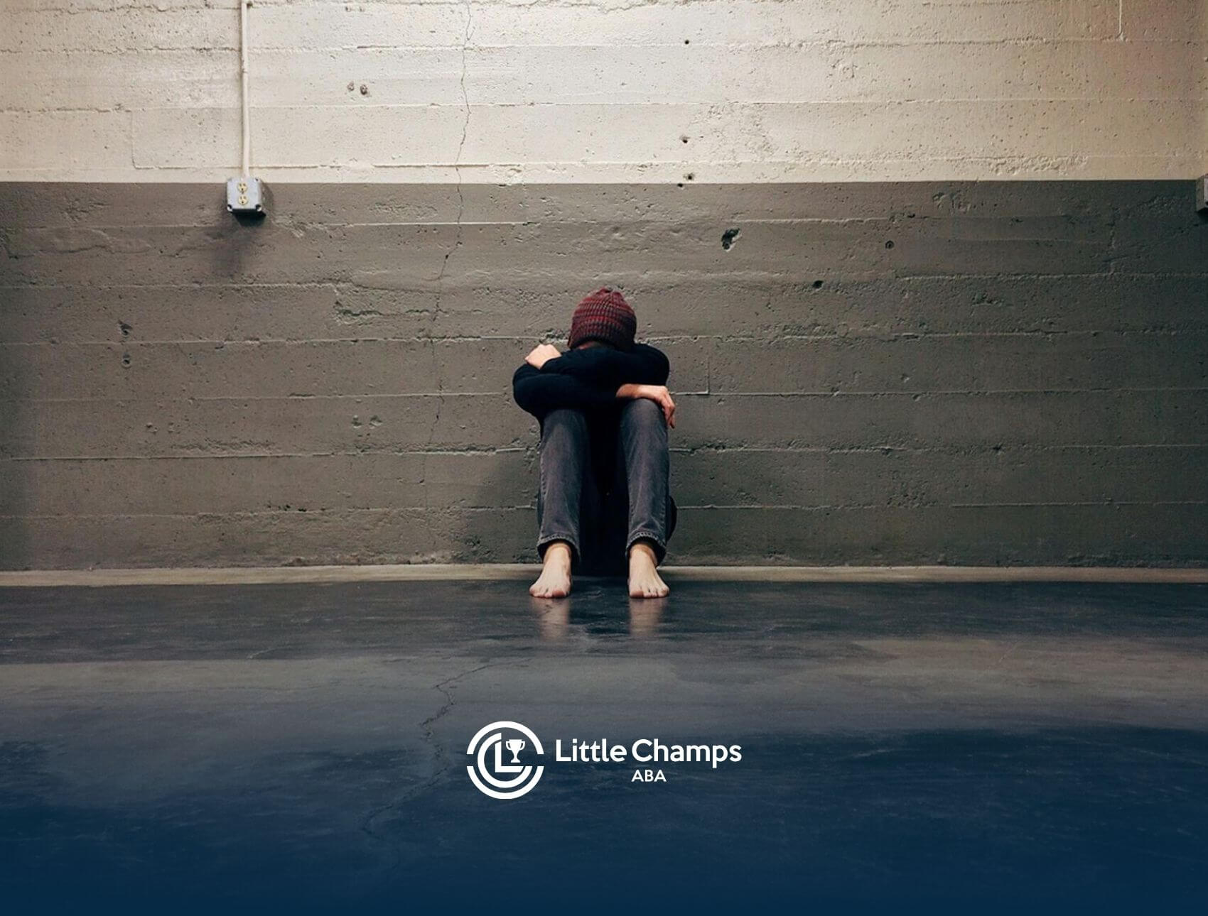 Autistic person sitting barefoot on the floor hugging knees while crying in an empty concrete room in Colorado.