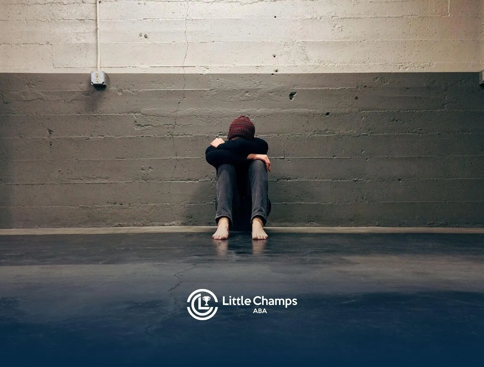 Autistic person sitting barefoot on the floor hugging knees while crying in an empty concrete room in Colorado.