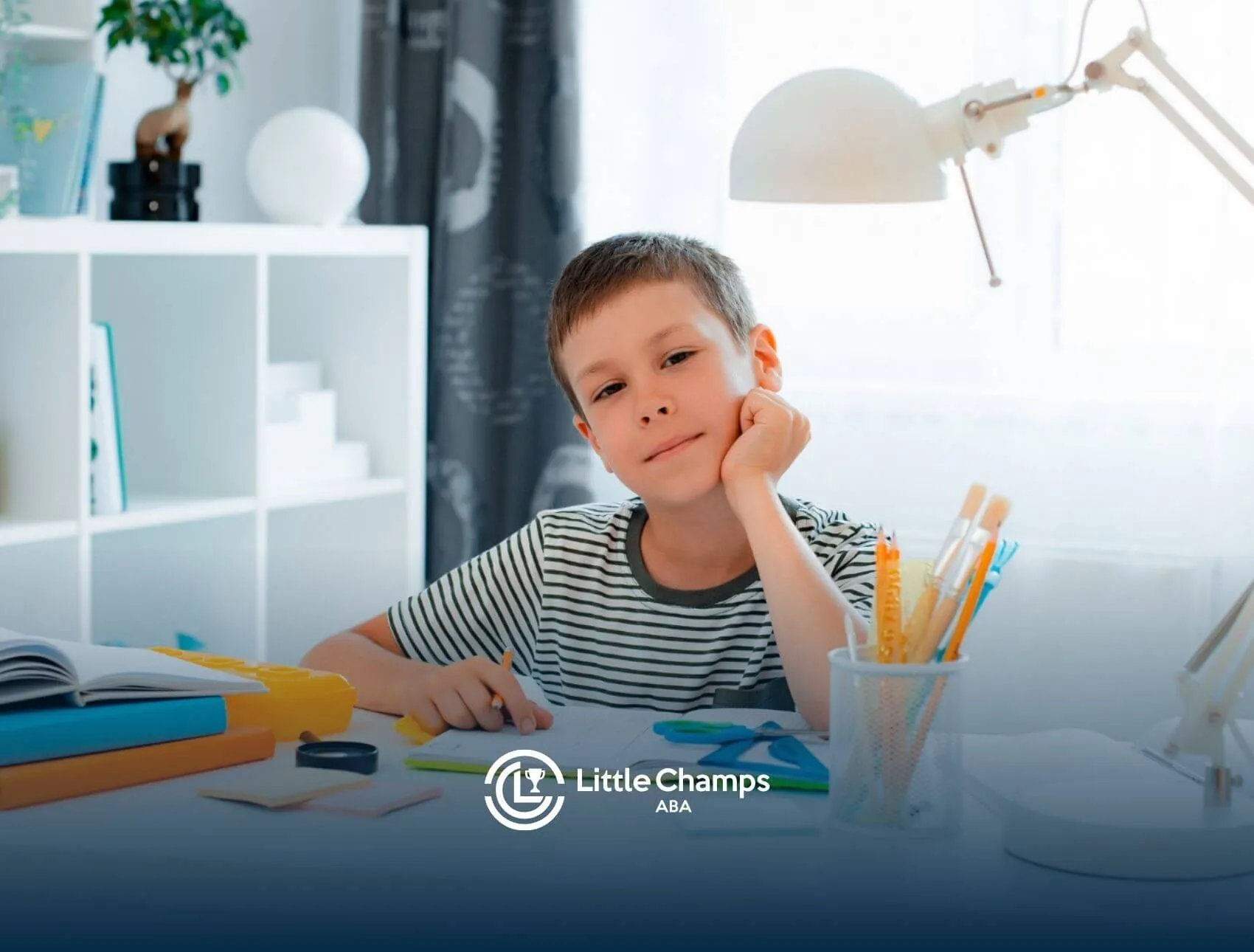 Young boy with autism sitting at a desk doing homework with school supplies around him.