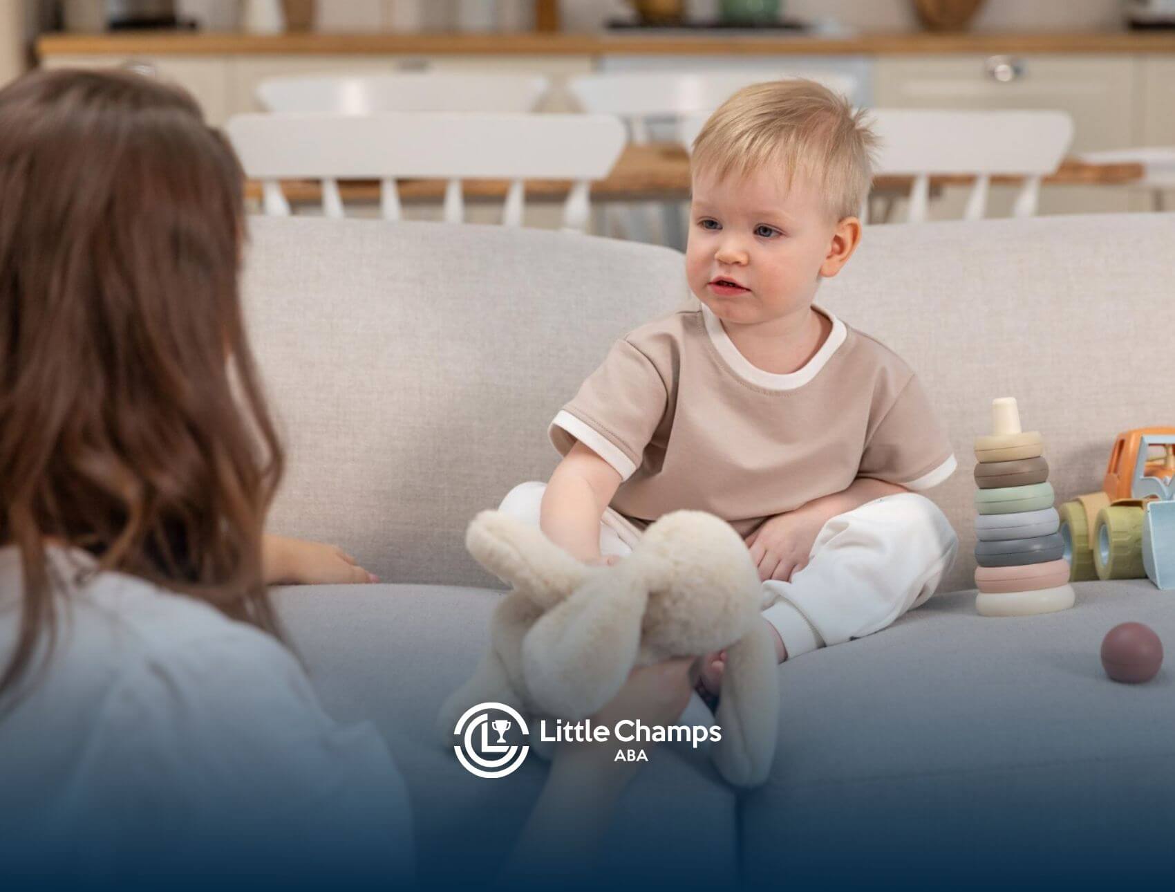 A toddler sitting on a couch playing with a stuffed animal and colorful toys.