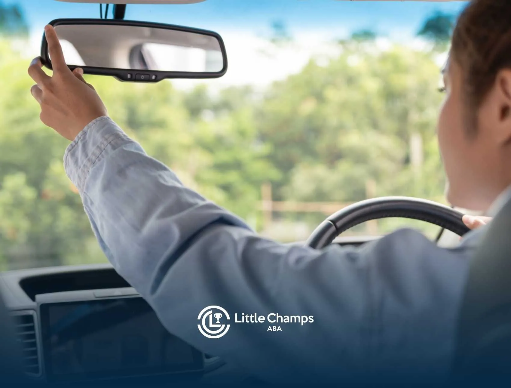 A person adjusts the rearview mirror of a car interior, focusing on green trees outside.
