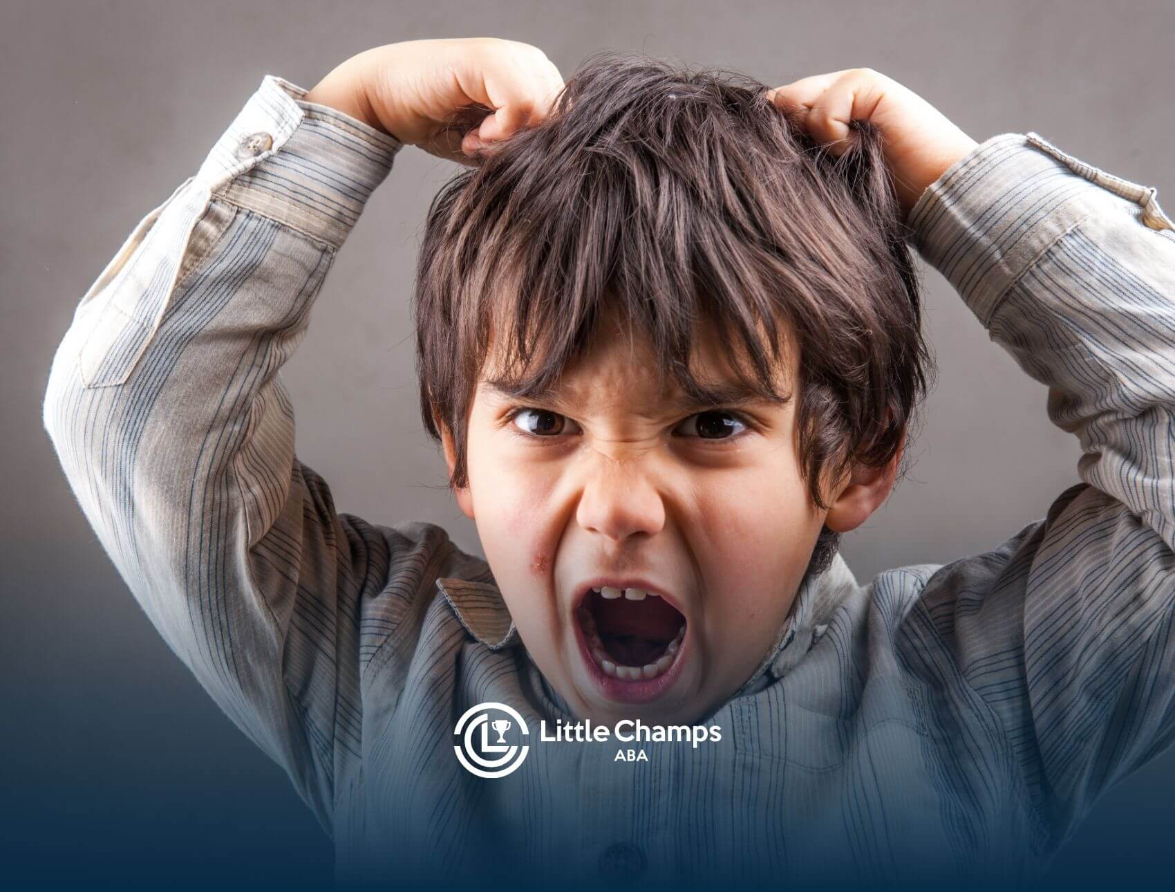A young autistic boy with messy hair, showing frustration while pulling his hair in distress during ABA therapy.