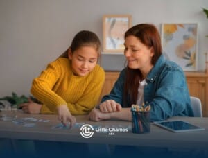 A female ABA therapist & a young autistic girl sitting at a table, playing with alphabet cards, sharing a moment of fun.