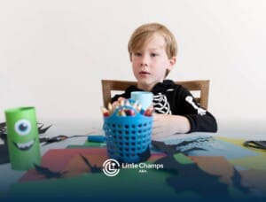 A young boy wearing a skeleton hoodie, sitting at a table surrounded by art supplies, looking focused.