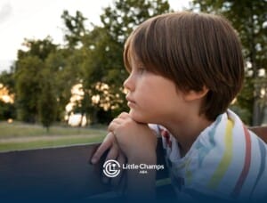 An autistic boy sitting on a park bench with his hands clasped, staring thoughtfully into the distance.