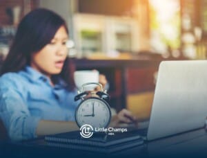 An ABA therapist working at her desk with a cup of coffee, an alarm clock, and a laptop, looking stressed.