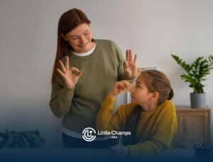 A BCBA using hand gestures while teaching a child with learning cards at a table during ABA therapy.