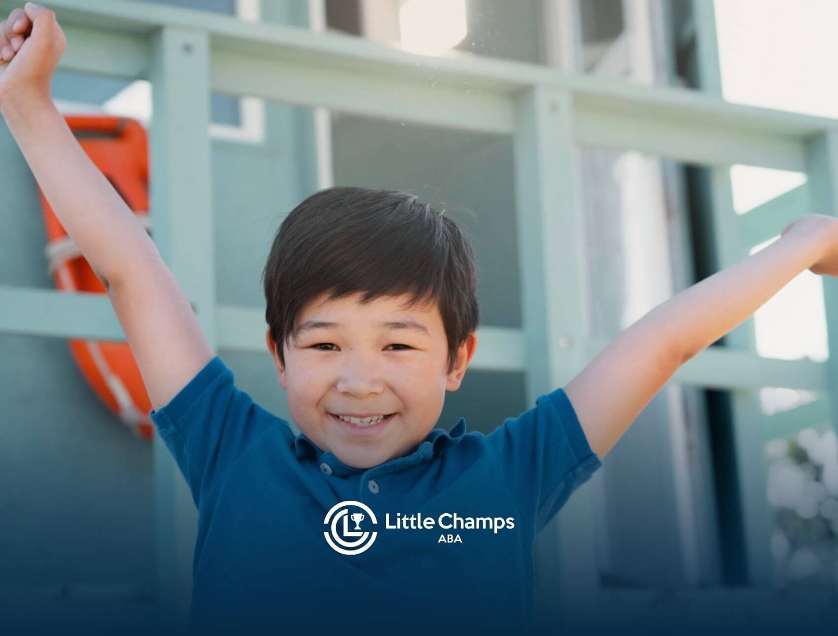 Happy young boy smiling with arms raised, possibly celebrating progress during ABA therapy session.