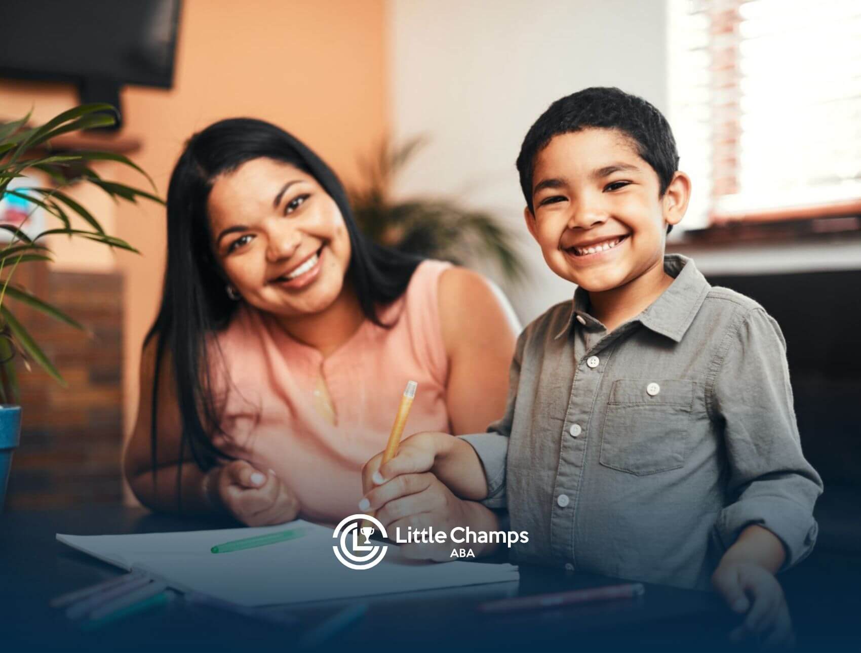 Smiling BCBA and young boy sitting at a table in ABA therapy.