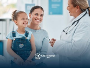 Smiling mother and daughter speaking with a doctor holding a syringe in a clinic.