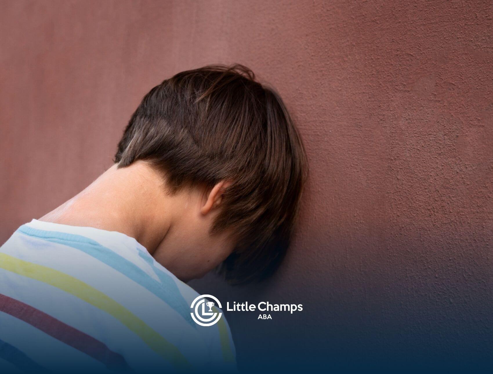 Back view of a child with autism leaning their forehead against a textured brown wall.