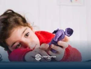 Young child with autism lying down while closely examining a small purple clay figure during ABA therapy.