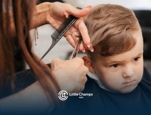 Hair stylist cutting a young child’s hair with scissors and a comb at a salon.