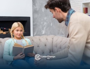 Girl with autism sitting on a couch reading a book while a BCBA speaks to her in ABA therapy.