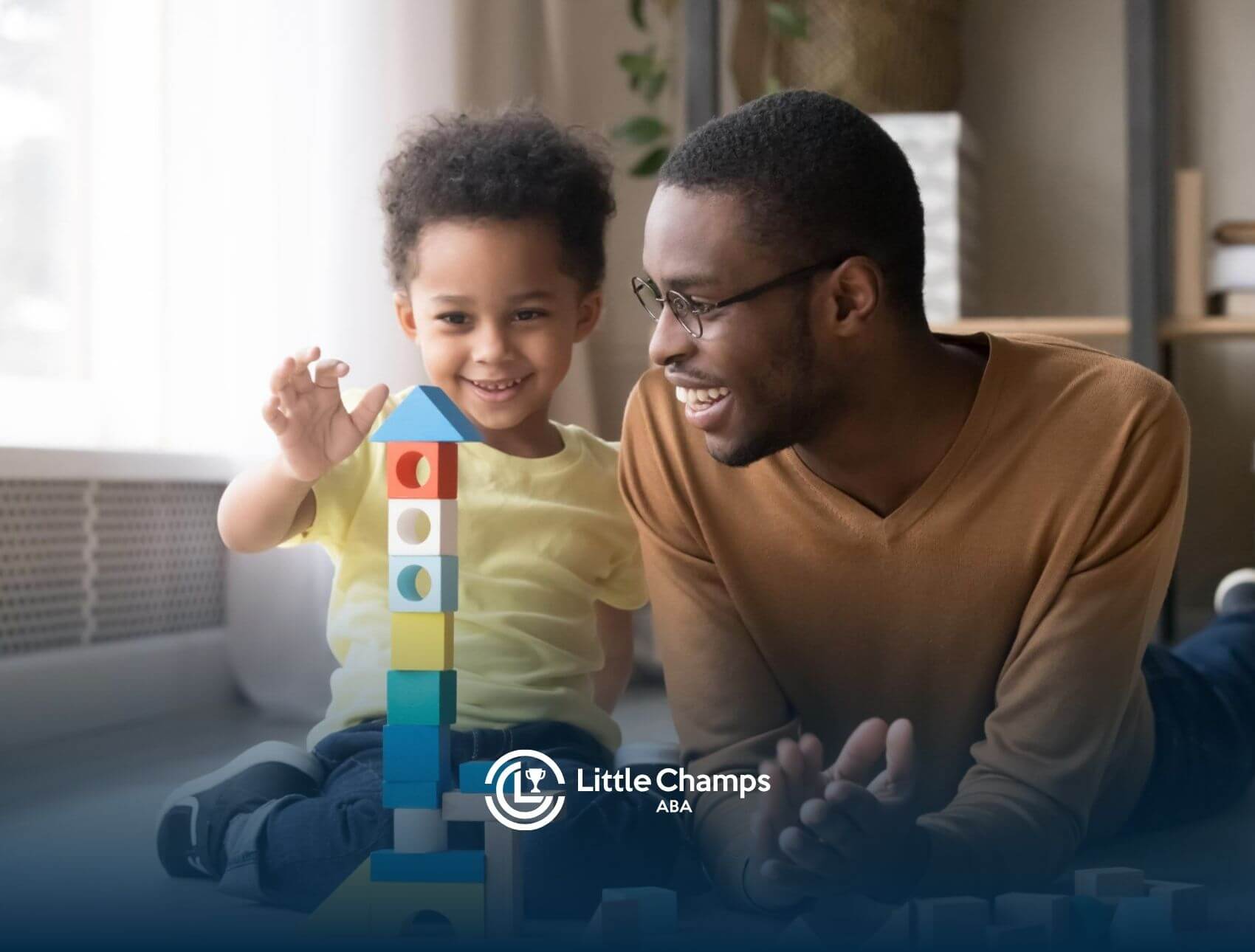 A smiling BCBA and young child with autism lying on the floor together during ABA therapy.