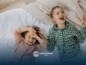 Two young children laughing together in bed during a fun sleepover.