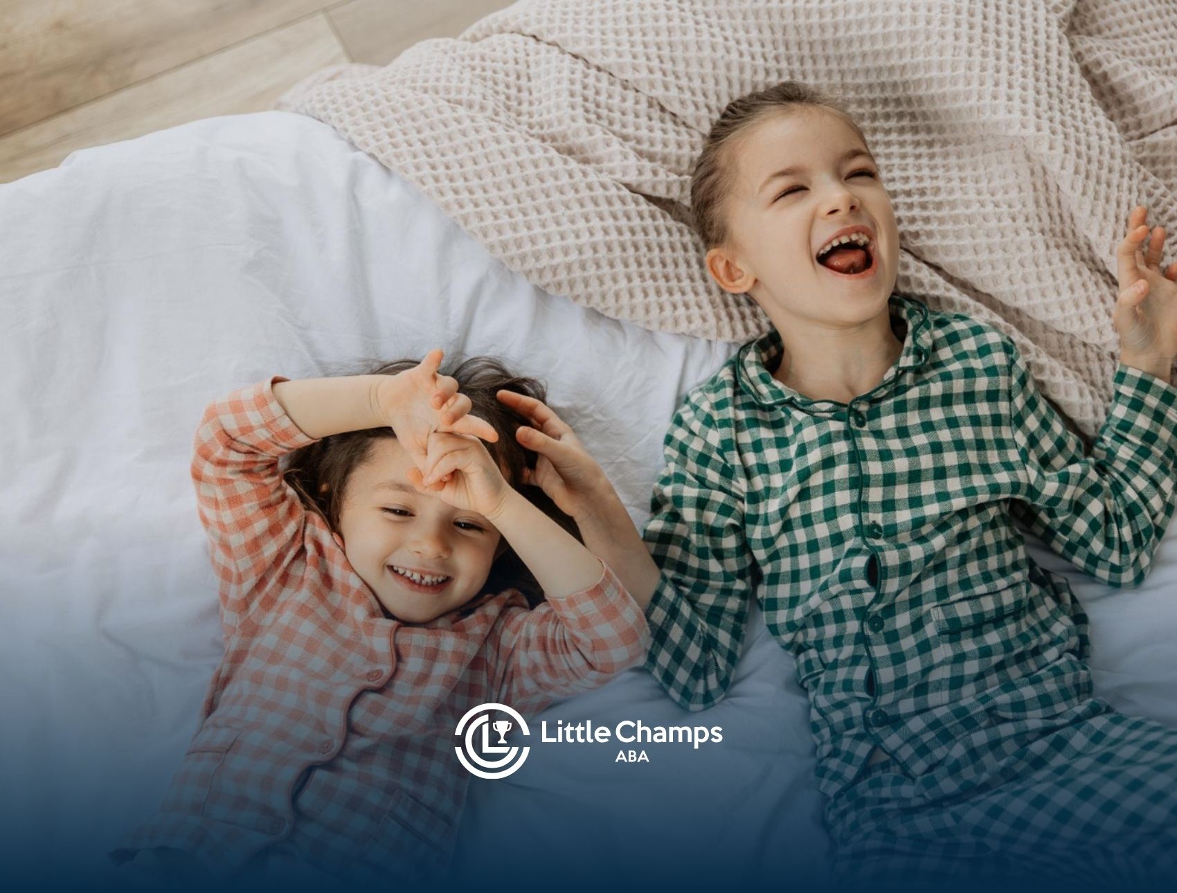 Two young children laughing together in bed during a fun sleepover.