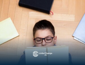 Young boy wearing glasses reading a book while lying on the floor.
